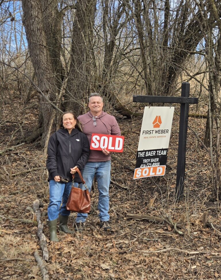 man and woman standing next to SOLD real estate sign