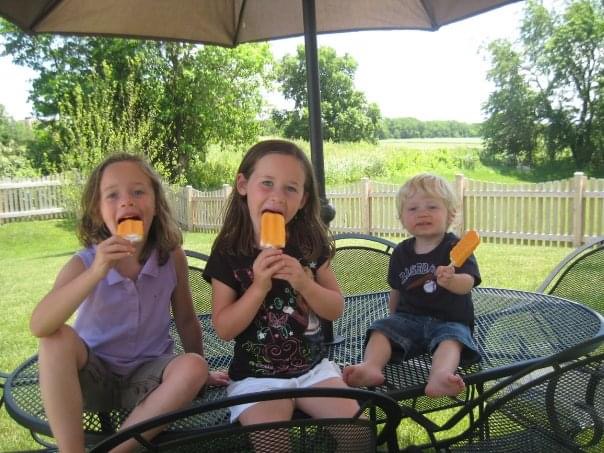kids eating popsicles at a table in backyard