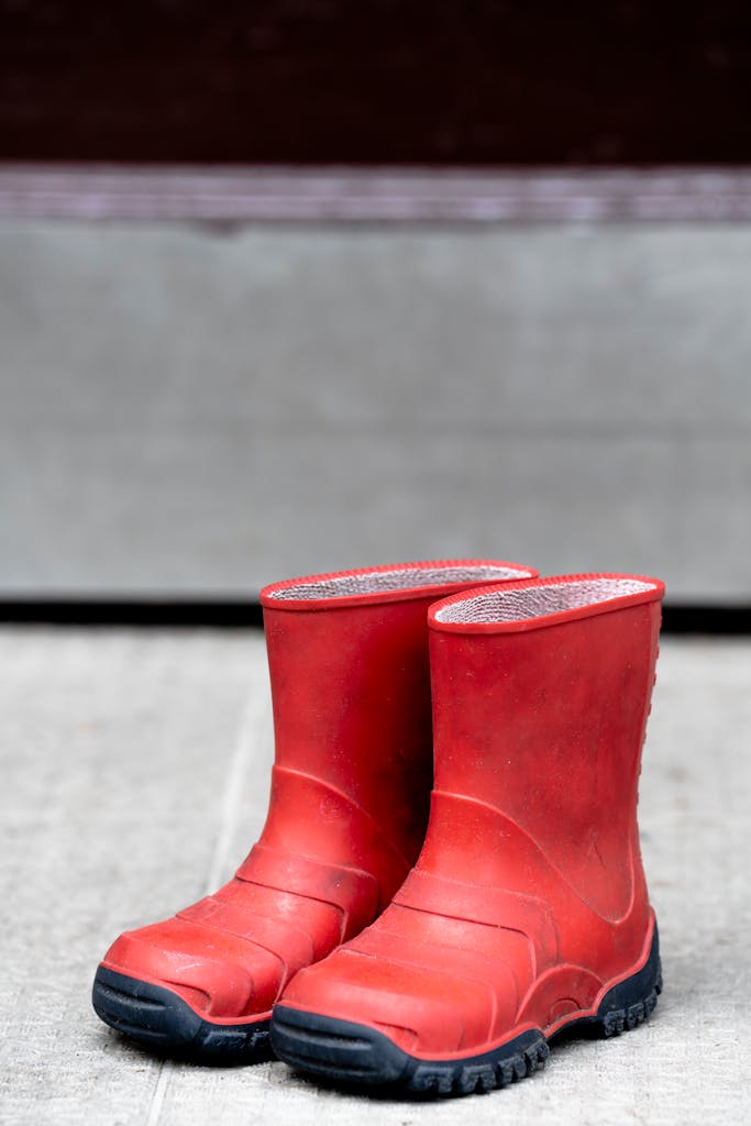 Bright red rubber boots standing on a concrete surface outdoors. Perfect for rainy seasons.