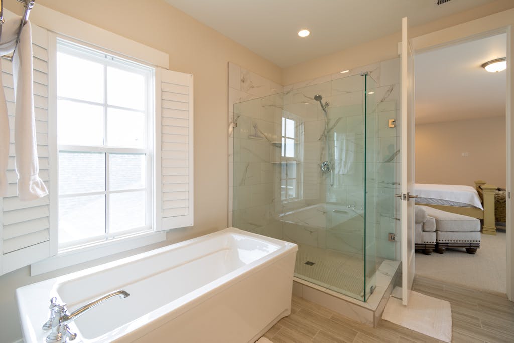 Bright modern bathroom with a bathtub and glass shower next to main floor primary suite.