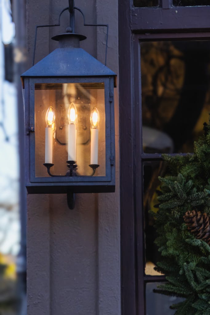 Outdoor lantern with three glowing candle-like bulbs on a building facade.